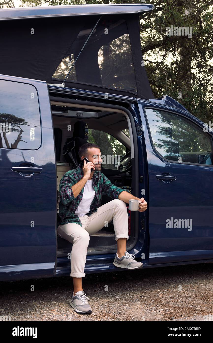 homme utilisant le téléphone assis dans la porte de son campeur Banque D'Images