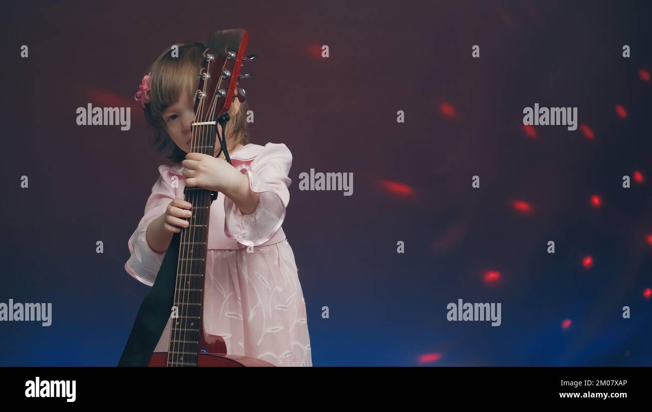 Petite fille dans une robe rose vintage joue une guitare acoustique comme une double basse Banque D'Images