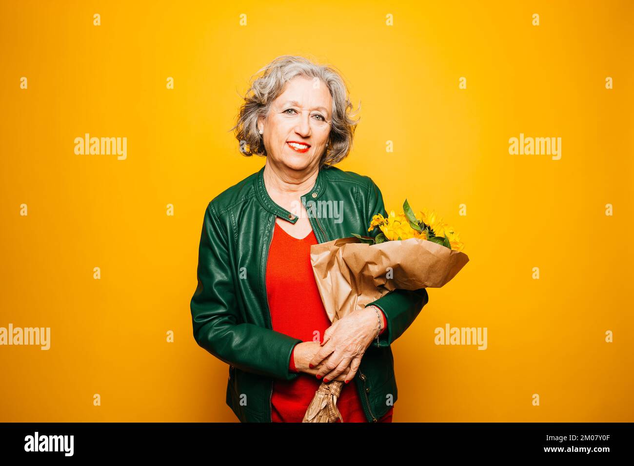 Portrait d'une femme âgée appliquant un rouge à lèvres sur un fond jaune Banque D'Images Portrait d'une femme âgée appliquant un rouge à lèvres sur un fond jaune Banque D'Images