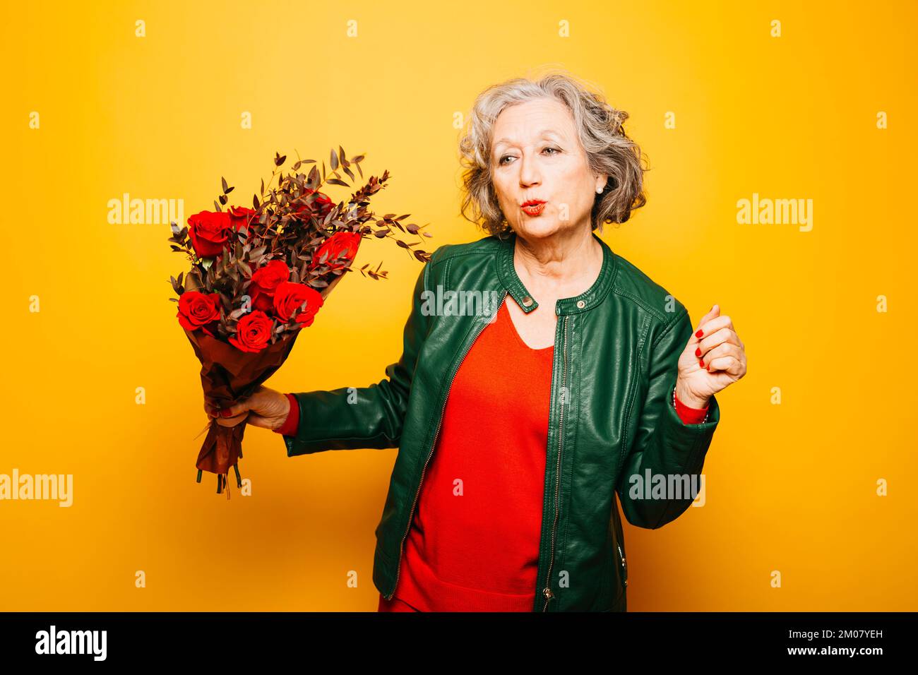 Portrait d'une femme âgée dansant avec un bouquet de roses rouges sur fond jaune Banque D'Images Portrait d'une femme âgée dansant avec un bouquet de roses rouges sur fond jaune Banque D'Images