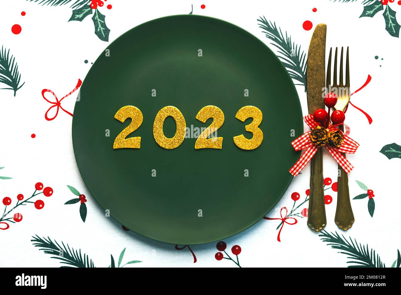 Bonne année 2023. Vue de dessus des numéros dorés 2023 sur l'assiette avec des couverts pour le dîner de Noël sur la nappe de noël. Célébration de la Saint-Sylvestre c Banque D'Images