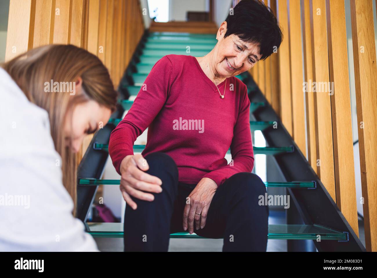 Femme âgée assise dans les escaliers, attendant patiemment que l'infirmière fixe ses chaussures Banque D'Images
