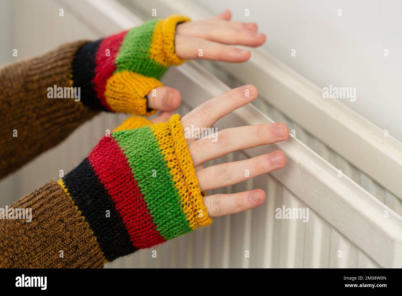 Gros plan des mains dans des gants sans doigts qui chauffent contre un radiateur à gaz Banque D'Images