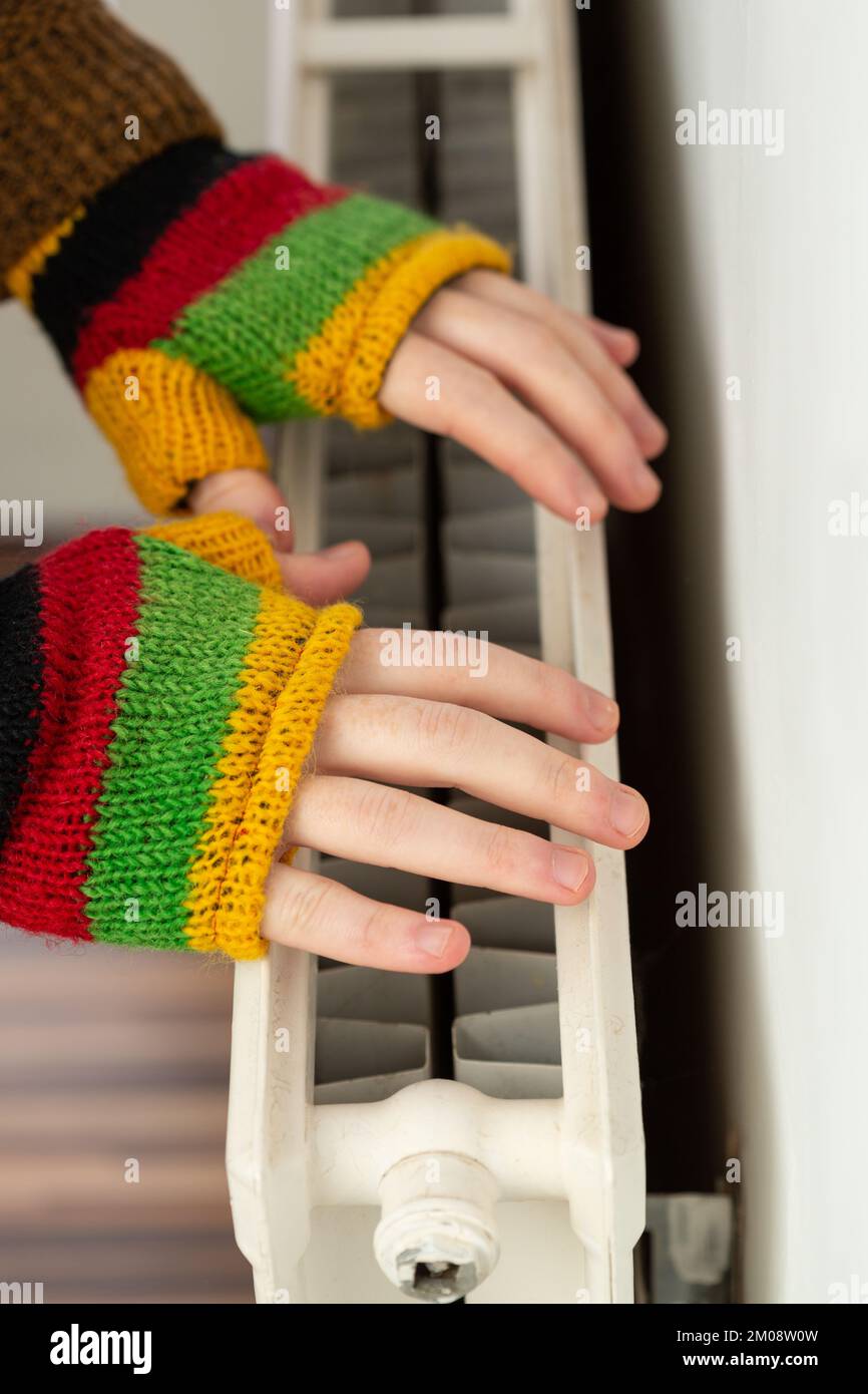 Gros plan des mains dans des gants sans doigts qui chauffent contre un radiateur à gaz Banque D'Images