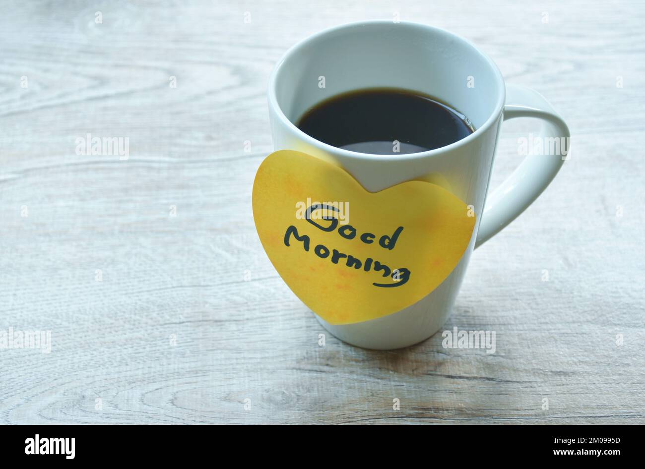 Tasse de café noir message du matin dans du papier coeur jaune sur la table Banque D'Images