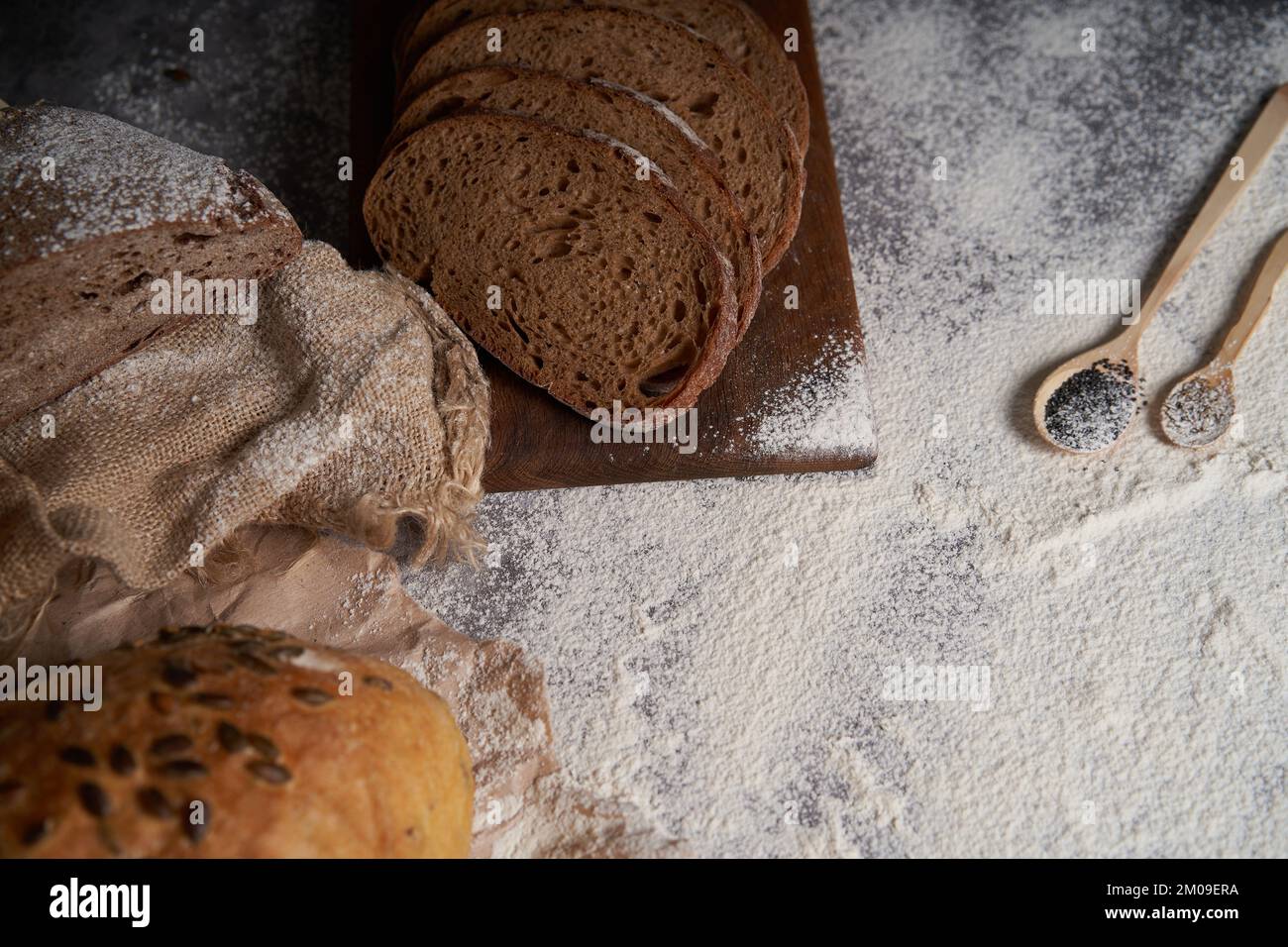 Vue de dessus de différents types de pain, tranché et entier, farine, papier froissé et toile de jute sur une table en bois. Angle élevé. Banque D'Images