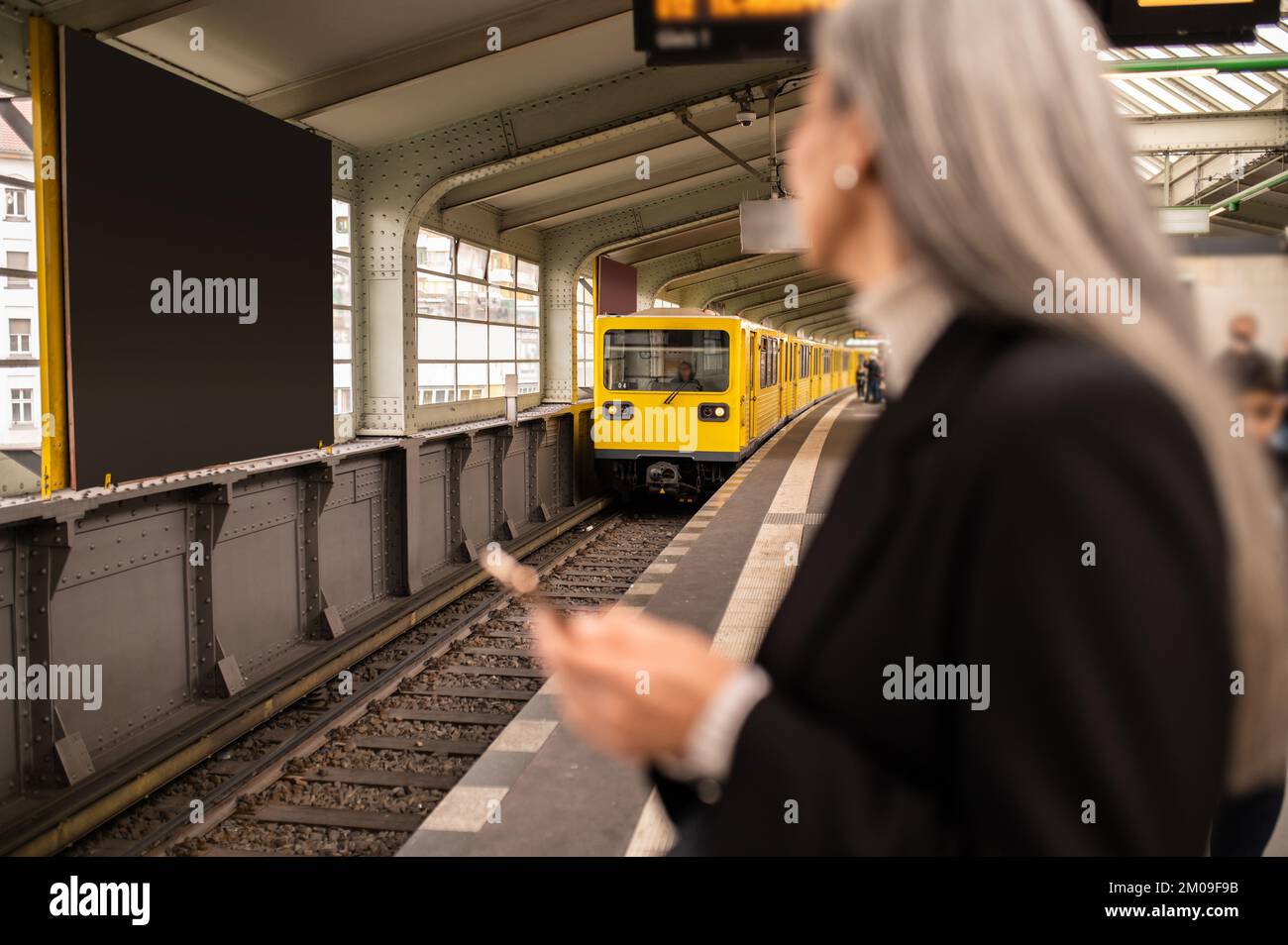 Femme aux cheveux longs vêtue d'un manteau noir attendant un train dans un métro Banque D'Images
