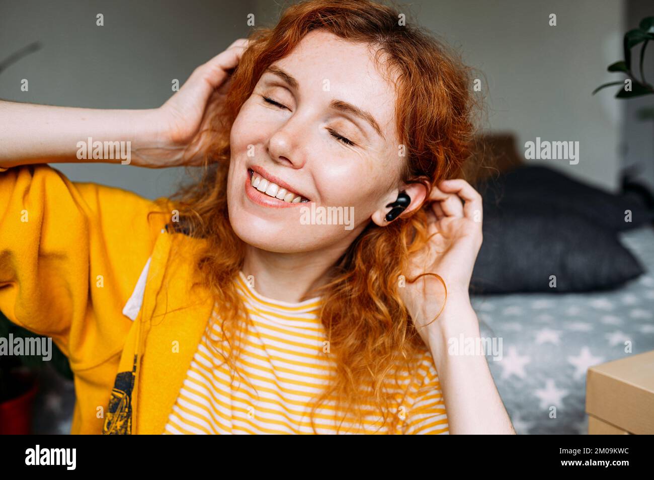 Bonne fille aux cheveux rouges écoutant de la musique, à la maison dans un casque sans fil Banque D'Images