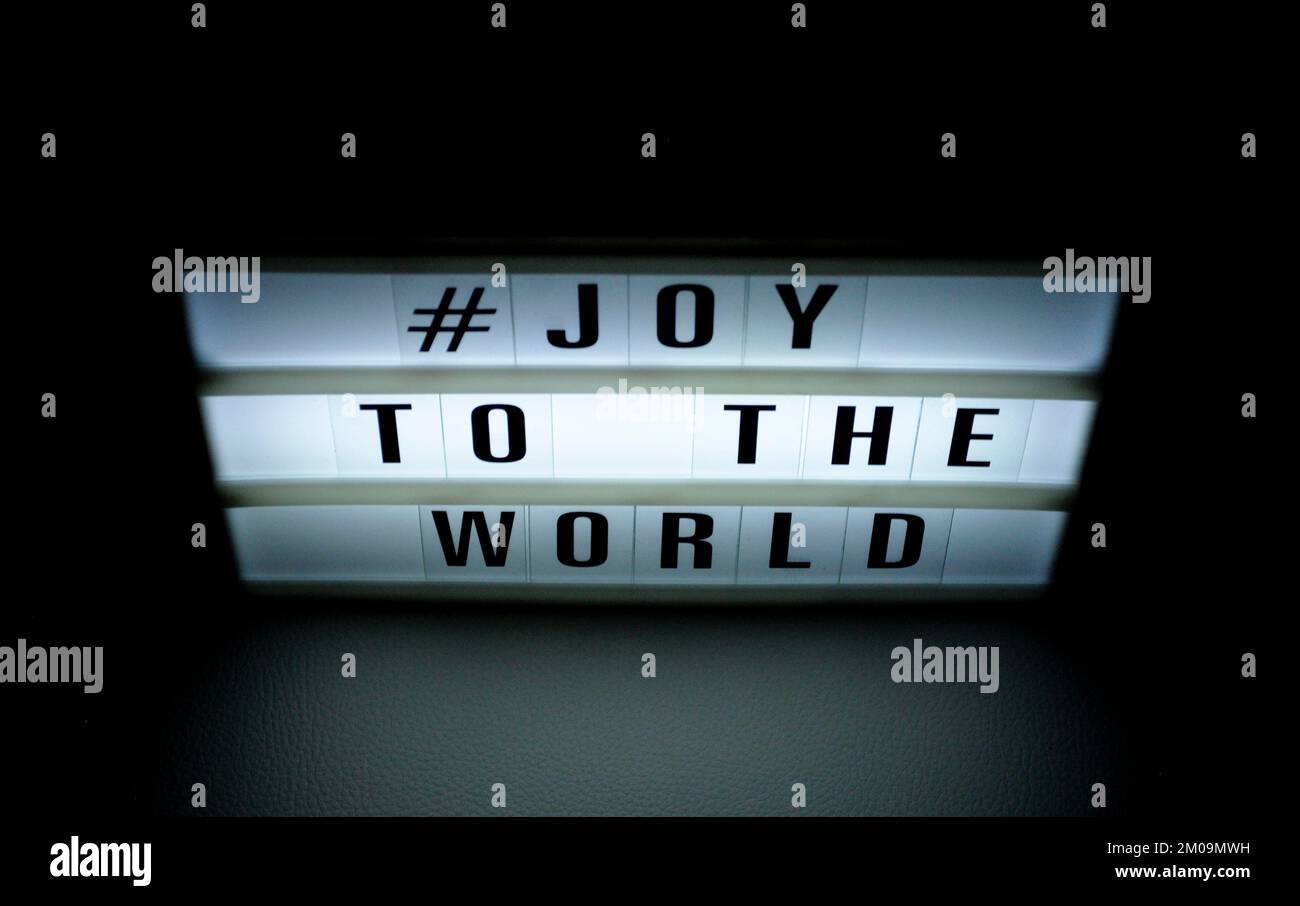 Boîte lumineuse avec l'expression « # Joy to the World » illuminée sur elle dans l'ombre et le fond sombre Banque D'Images