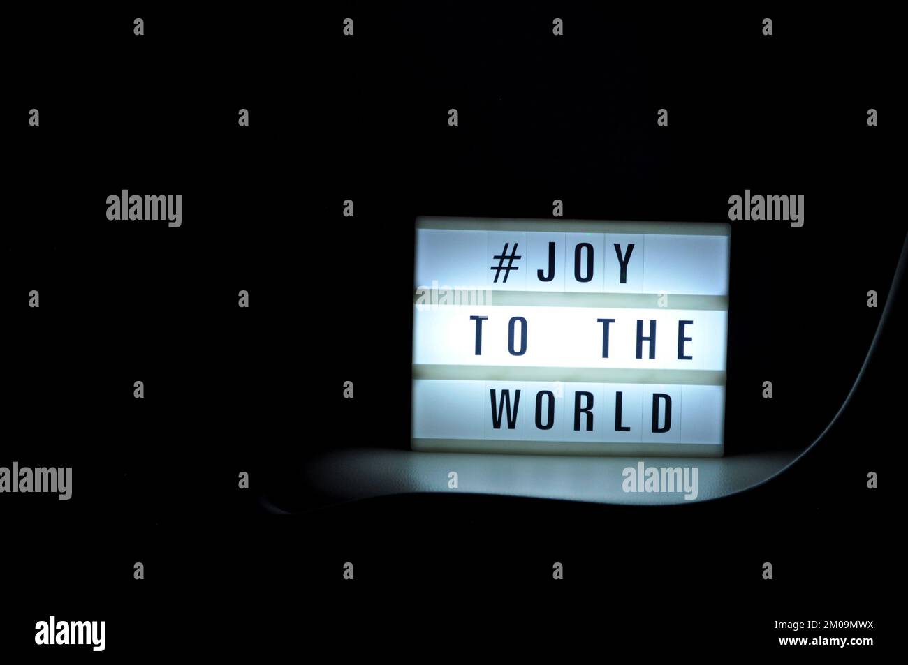 Boîte lumineuse avec l'expression « # Joy to the World » illuminée sur elle dans l'ombre et le fond sombre Banque D'Images