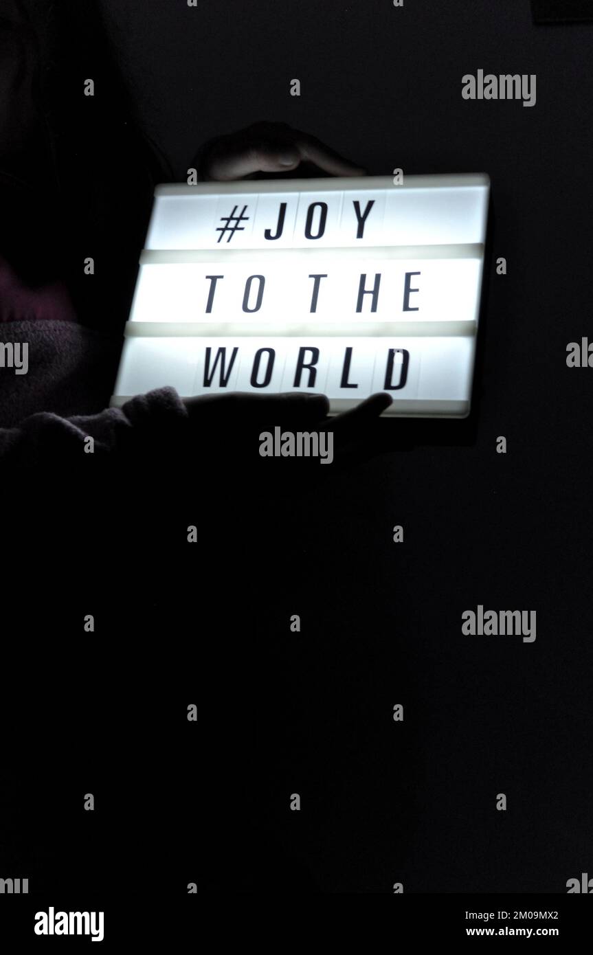 La boîte de lumière est tenue avec l'expression « # Joy to the World » illuminée sur elle dans l'ombre et le fond sombre Banque D'Images