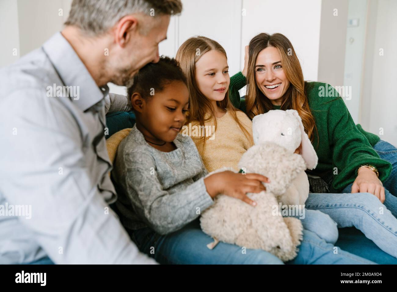 Une famille heureuse assise sur un canapé, des sœurs adoptées jouant des jouets en peluche. Concept d'adoption. Banque D'Images