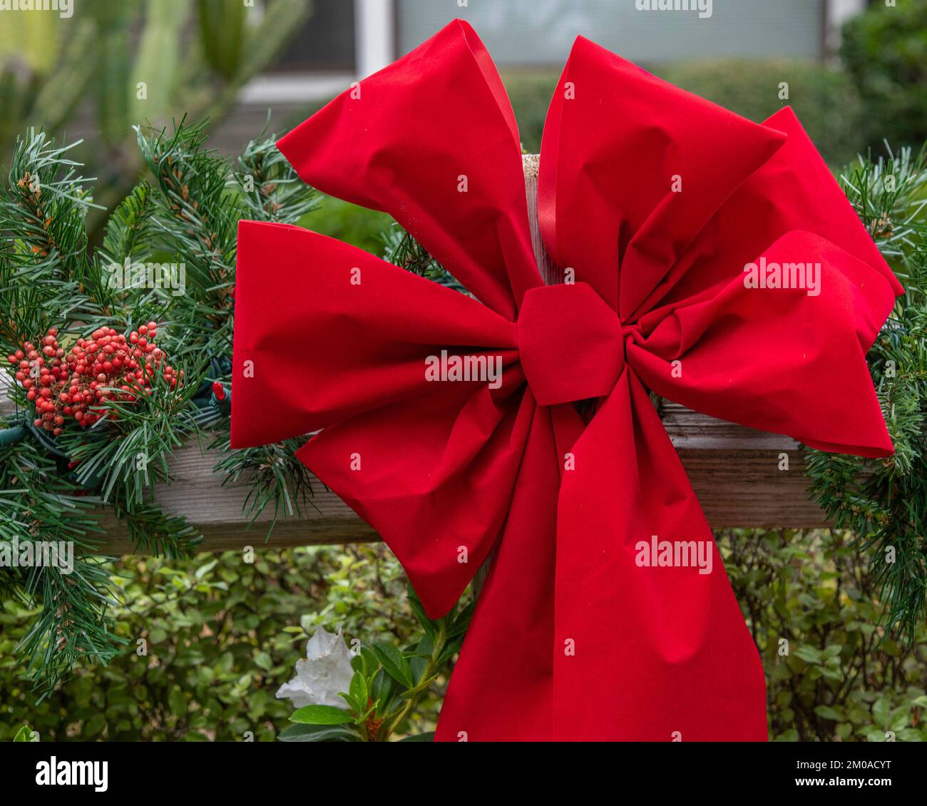Gros plan d'une couronne de Noël toujours verte avec un ruban rouge accroché à un poteau de clôture. Banque D'Images