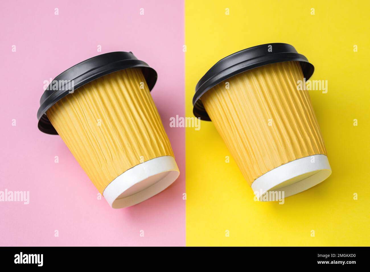 Gros plan de deux tasses à café ou à thé jaunes à emporter placées parallèlement et inclinées vers la gauche sur une table ou un papier coloré. Fond rose. Copier l'espace pour le texte. Mise au point sélective douce Banque D'Images