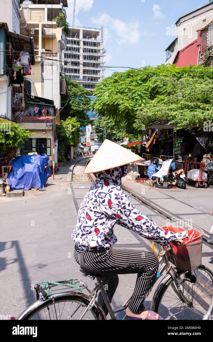 Hanoï, Vietnam - 16 septembre 2018 : une jolie femme vietnamienne avec une adresse traditionnelle traverse la piste du train sur un vélo Banque D'Images