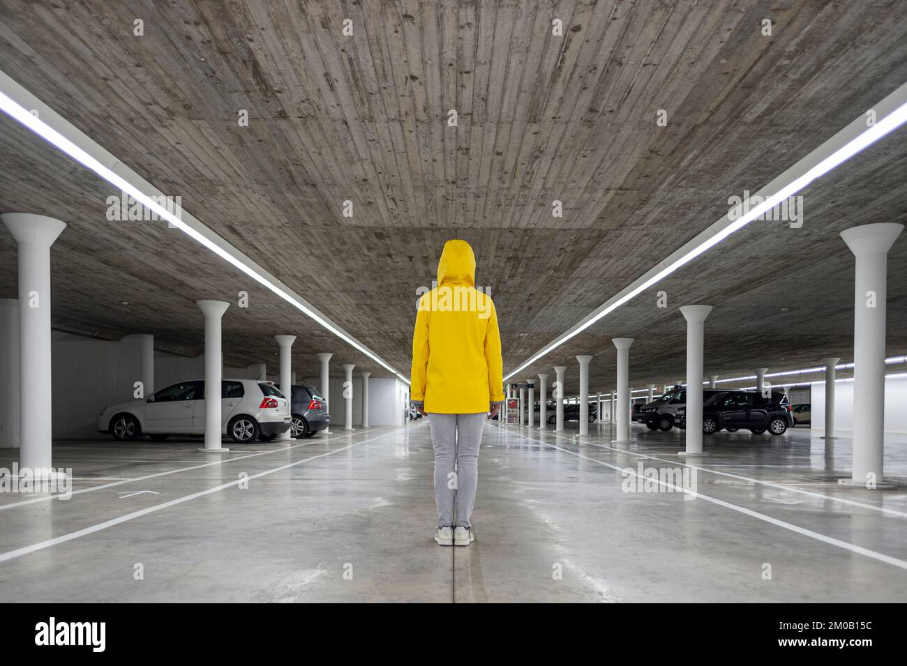Personne revêtant un manteau jaune avec une capuche debout dans un parking souterrain, vue arrière Banque D'Images