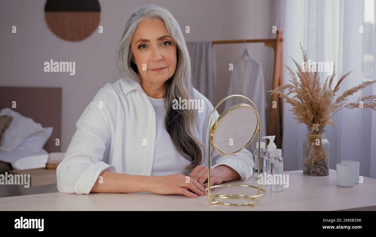 Vieille caucasienne magnifique dame 60s femme sourire senior femme mûre avec miroir à la maison regardant l'appareil photo grand-mère modèle 50s appréciez la peau du visage rides Banque D'Images