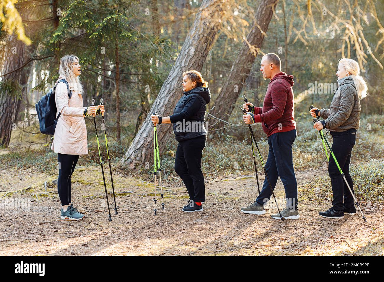Une femme sérieuse avec un groupe de personnes enseigne les exercices scandinaves de marche avec des bâtons dans la forêt, expliquez les règles Banque D'Images