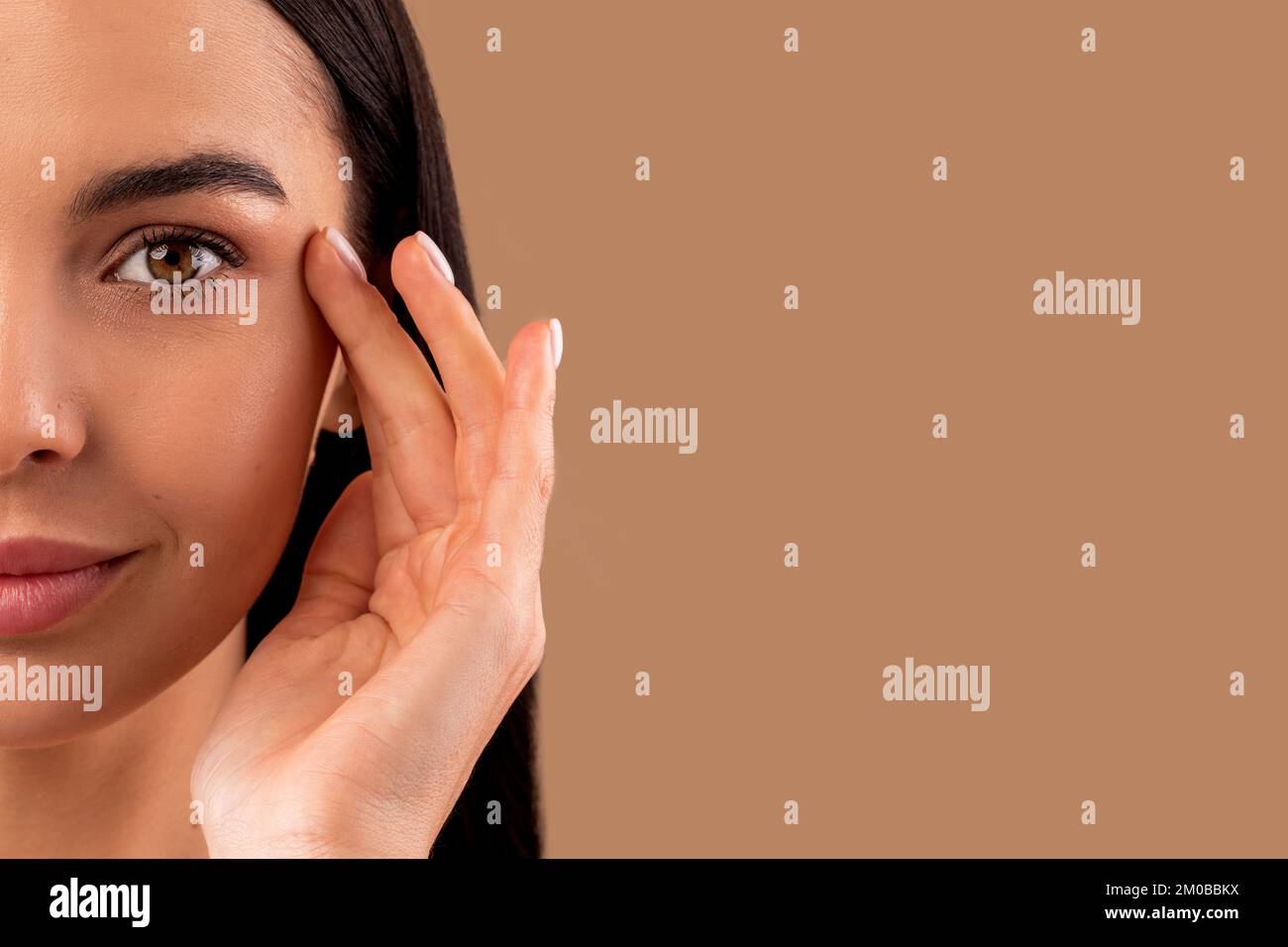 Demi-visage d'une belle femme brunette se touchant sous la peau des yeux Banque D'Images