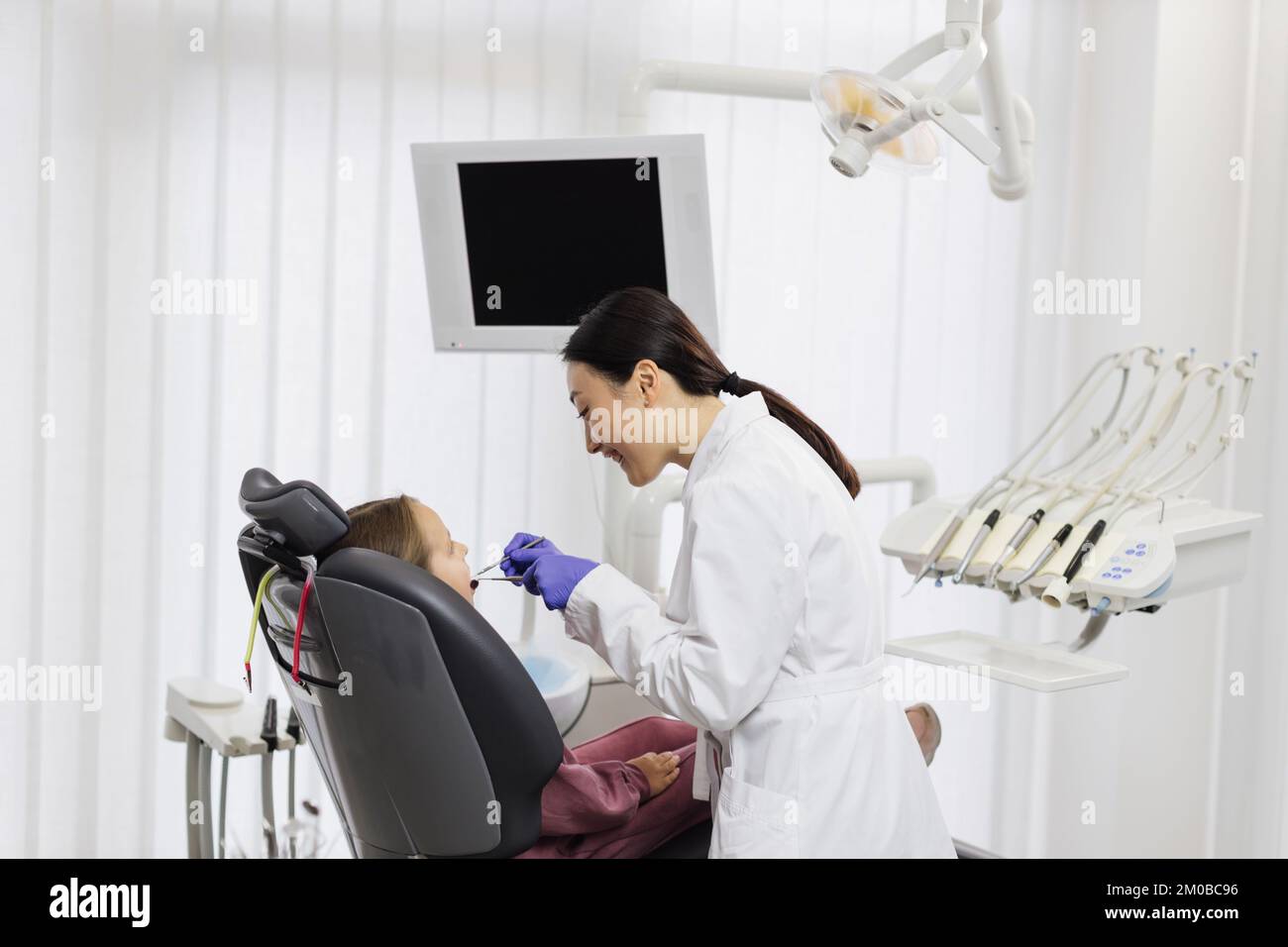 Un beau sourire aux dents blanches. Le dentiste asiatique examine la cavité buccale d'une jeune belle fille à travers une loupe dans le cabinet dentaire. Banque D'Images