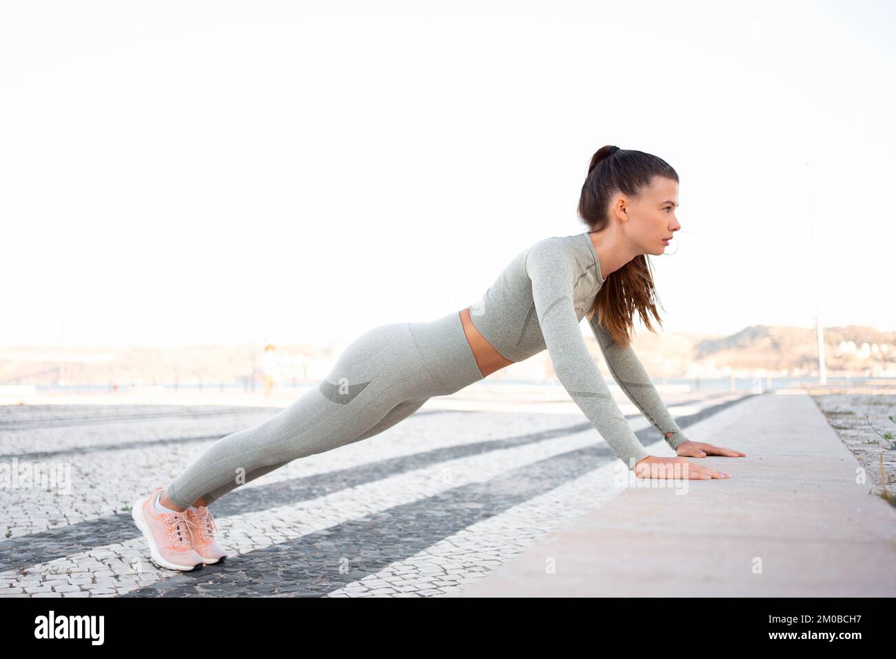 Jeune fille attirante athlète dans les vêtements de sport effectuant des push-up sur le pas de béton. Position des mains larges sur la photo, aspect stressé. Torse, poitrine, épaules et mains affectant l'exercice Banque D'Images