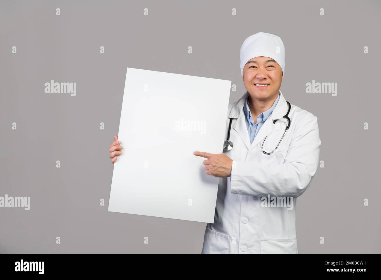 Joyeux thérapeute chinois mature en manteau blanc avec stéthoscope tenir la bannière avec l'espace de copie Banque D'Images