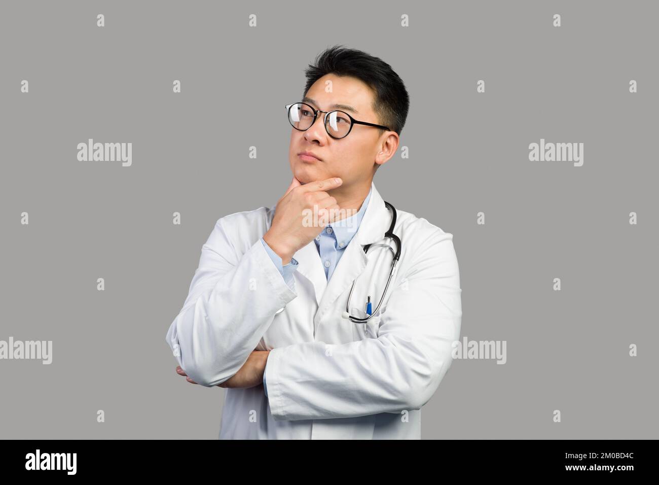 Pensive mature chinois Guy thérapeute dans le manteau blanc et des lunettes pense et regarde l'espace libre Banque D'Images