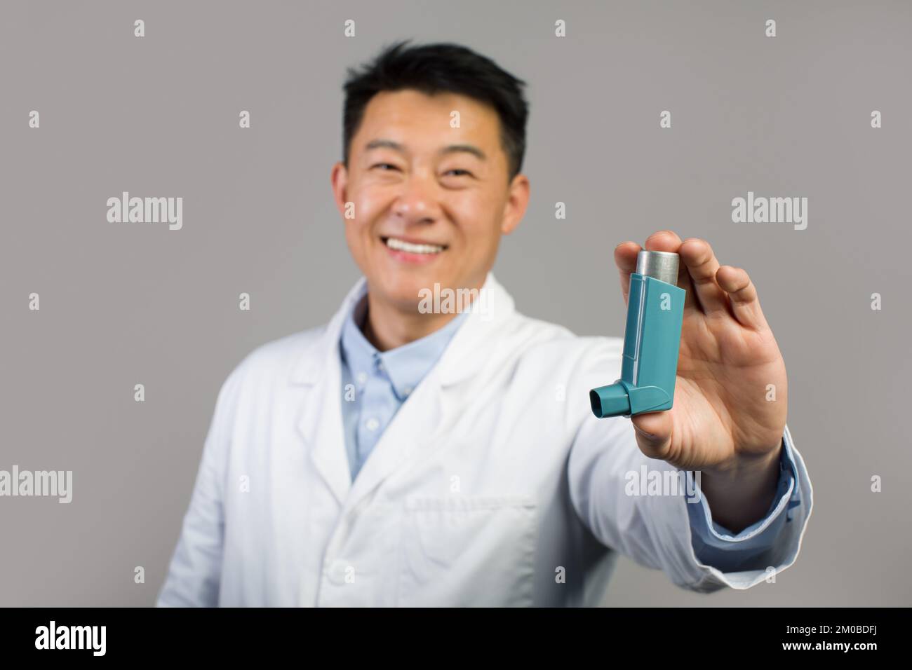 Thérapeute chinois mature souriant en manteau blanc montrant un inhalateur pour la respiration et l'attaque asthmatique Banque D'Images