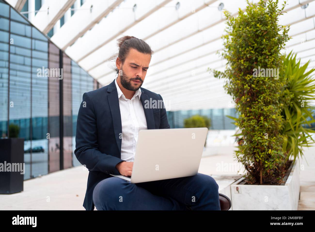 Homme d'affaires en déplacement travaillant sur son ordinateur portable dans la rue près du bureau. Une personne d'affaires hispanique élégante assise utilise un ordinateur portable. Homme confiant gérant travaillant à l'extérieur. Banque D'Images