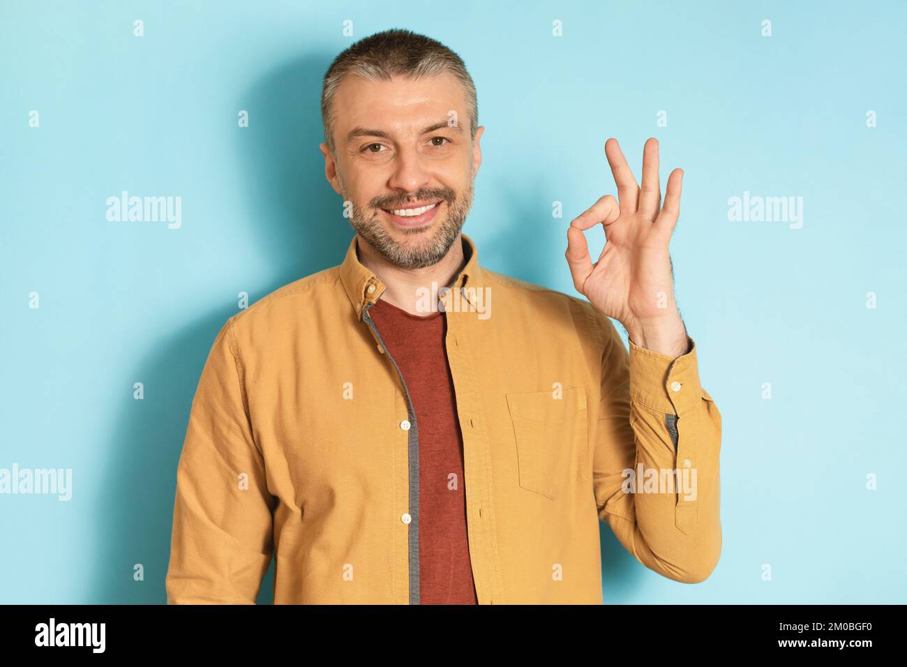 Je vais bien. Portrait d'un homme mûr heureux faisant l'approbation ok geste et souriant à l'appareil photo sur fond bleu studio Banque D'Images