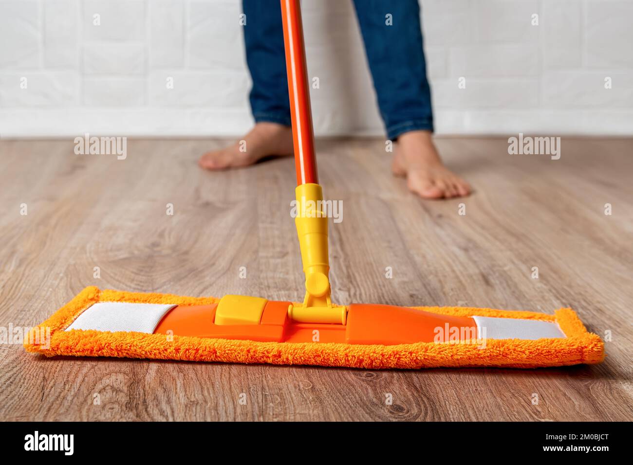 Une femme pieds nus se moque du sol. Nettoyage des sols stratifiés en bois pour femmes avec un balai en microfibre orange à la maison. Les devoirs, le ménage, le nettoyage. Banque D'Images