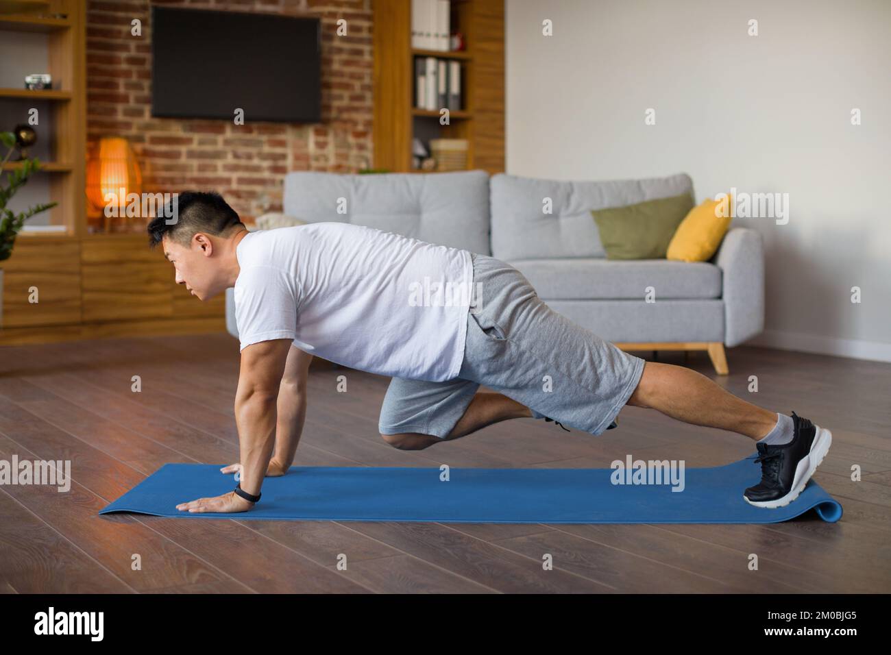 Homme asiatique mature actif faisant des exercices de alpinistes de cross-corps sur tapis de fitness, l'entraînement dans l'intérieur de salon Banque D'Images