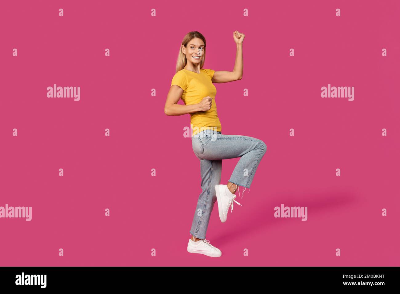 Gaie femme blonde de race blanche d'âge moyen en t-shirt jaune faisant la victoire et le geste de succès Banque D'Images