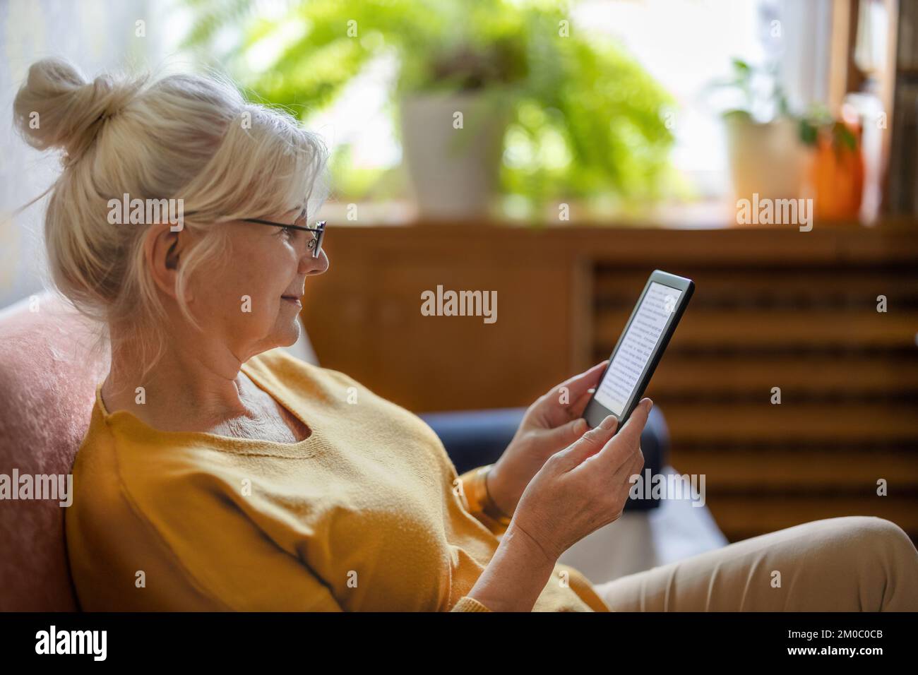 Femme âgée utilisant un lecteur électronique et lisant un livre électronique à la maison Banque D'Images