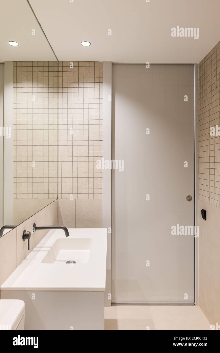 Vue verticale sur la salle de bains étroite et minimaliste. Grand miroir et lavabo blanc avec robinet noir. Banque D'Images