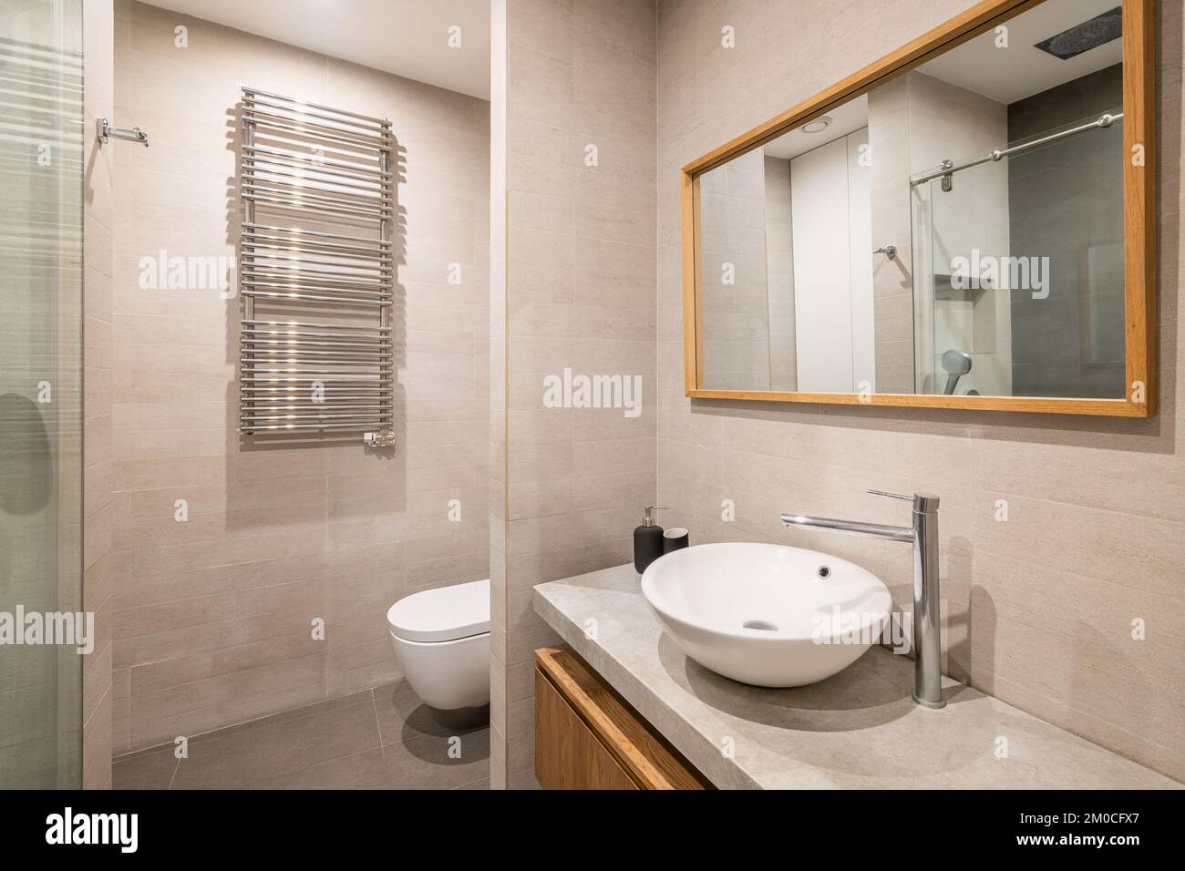 Intérieur de salle de bains moderne carrelée avec toilettes blanches, radiateur et douche en reflet de miroir encadré en bois. Banque D'Images