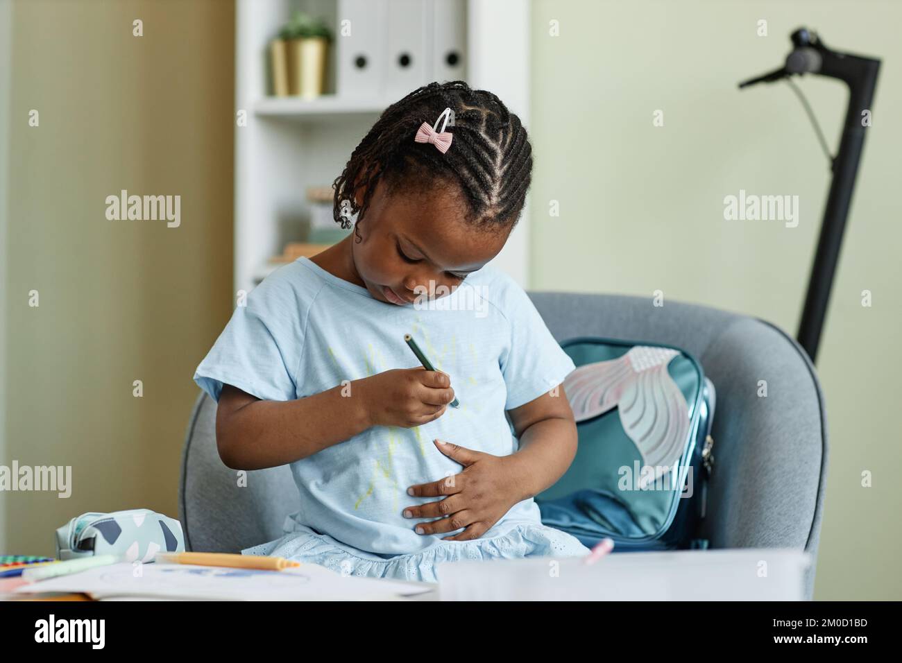 Portrait de petite fille noire dessinant sur la chemise tout en étant assis au petit bureau Banque D'Images