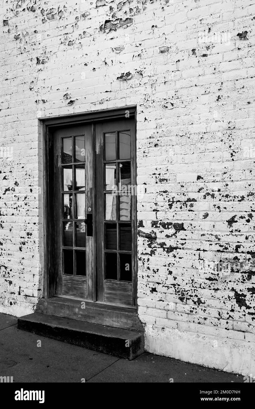 Une patina d'un âge sur une porte peinte avec un pas vers le trottoir dans un bâtiment en brique avec peeling, peint en blanc funky sur un mur en brique à Tucson, AZ, en B&W. Banque D'Images