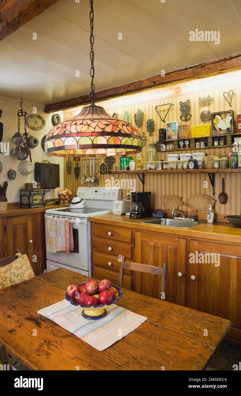Cuisine avec cuisinière rétro et table antique, comptoir et pots d'épices sur les étagères à l'intérieur de la vieille maison de style Cottage Canadiana de circa 1810. Banque D'Images