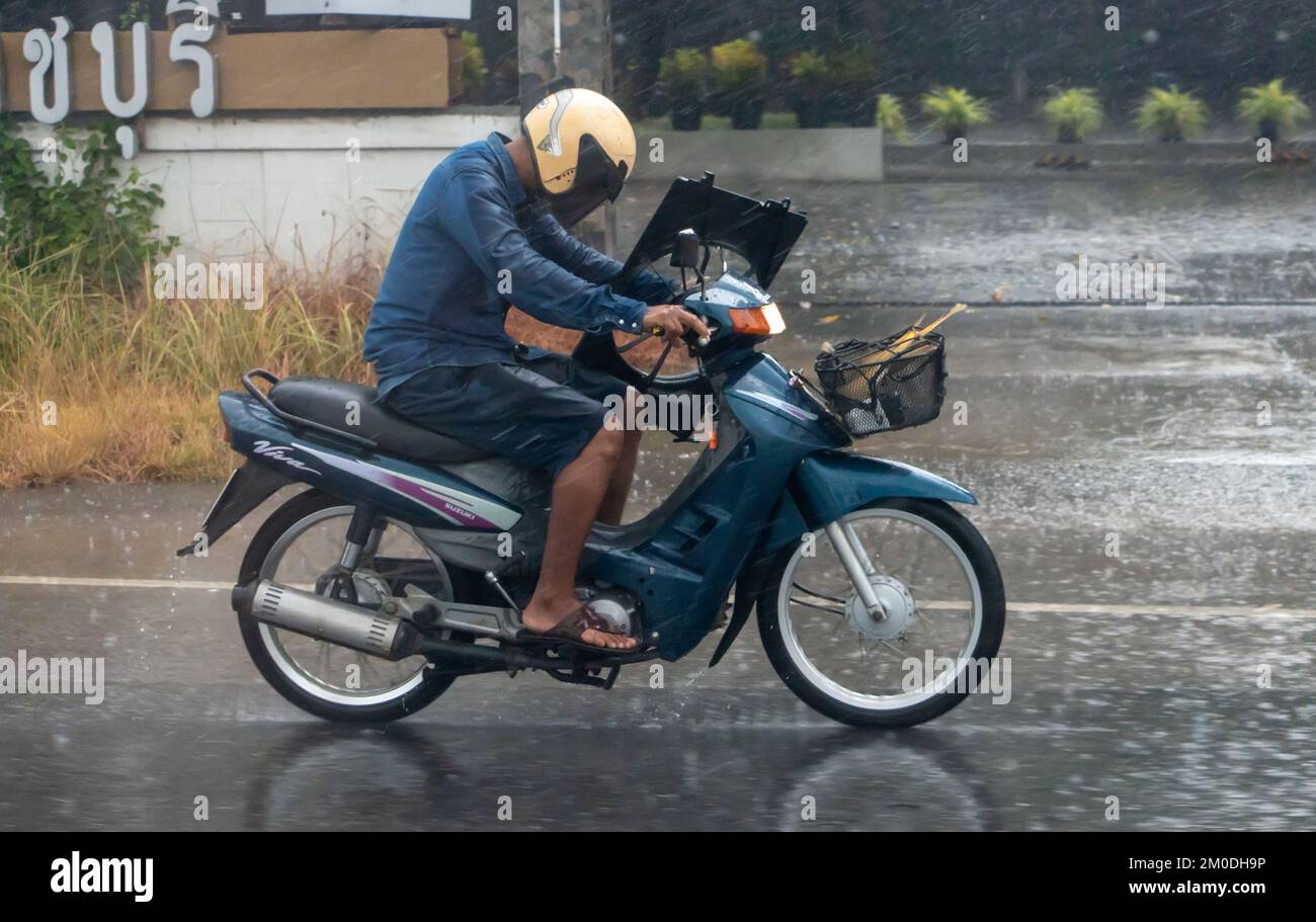 Ratchaburi, Thaïlande, NOVEMBRE 14 2022, Un homme avec une charge fait une moto sous la pluie Banque D'Images