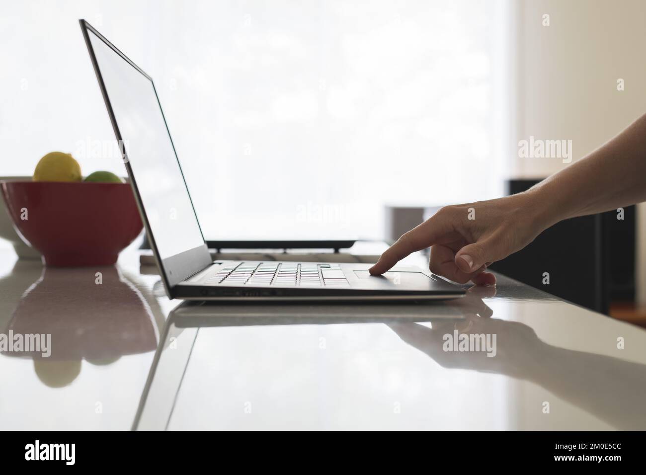 Gros plan de la main féminine défilant sur le tapis de souris de l'ordinateur portable moderne. Femme utilisateur d'ordinateur sur ordinateur portable au banc de cuisine. Banque D'Images