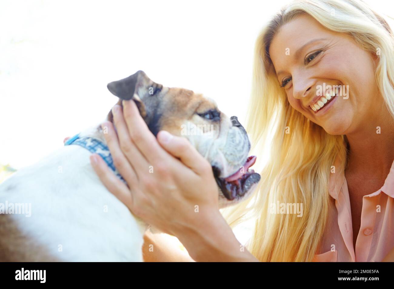 L'ami le plus fidèle que tout le monde pourrait avoir. Une blonde heureuse riant en jouant avec son chien à l'extérieur. Banque D'Images