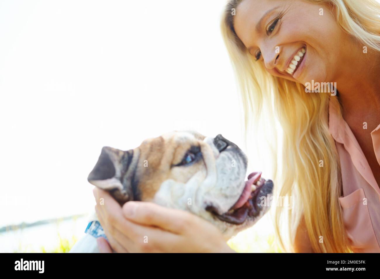 Passer du temps avec mon meilleur ami. Une blonde heureuse riant en jouant avec son chien à l'extérieur. Banque D'Images
