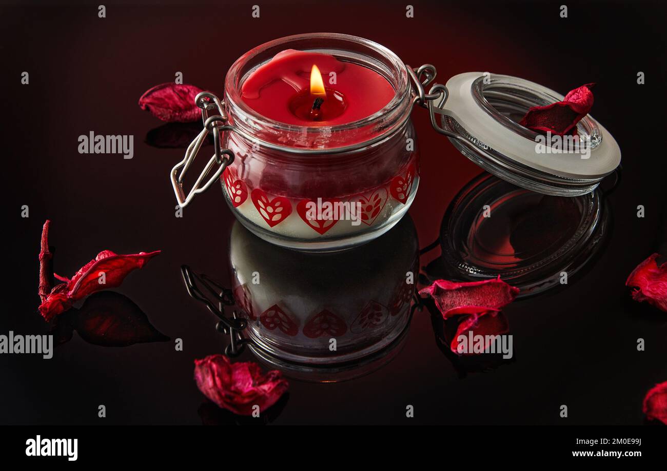 Bougie éclairée sur fond noir avec pétales de rose, vanille, cerise, grenade et arômes de noix de coco. Banque D'Images