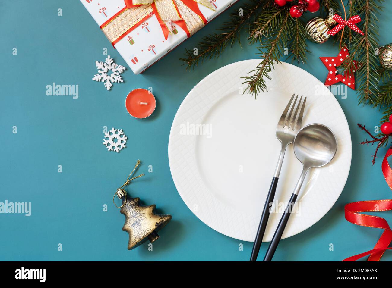 Plat de mise en place de table de Noël avec assiette, couverts, boîtes cadeaux et décorations de noël sur fond vert. Banque D'Images