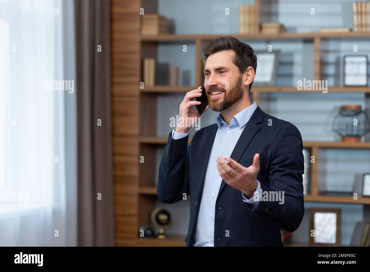 Un homme d'affaires mature qui parle au téléphone souriant et heureux, homme d'affaires en costume, travaillant dans un bureau classique. Banque D'Images