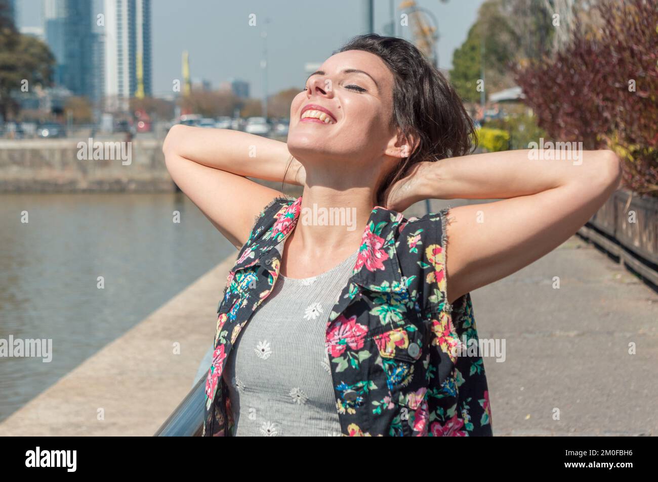 femme touriste caucasienne adulte avec les yeux fermés et souriant est détendue avec ses mains derrière son cou, respirer de l'air frais et se promener dans la ville. Banque D'Images