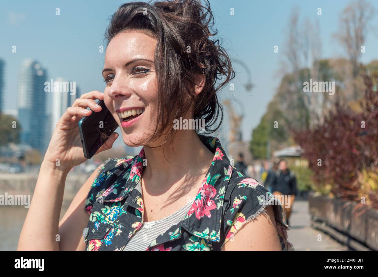belle femme caucasienne adulte, elle est heureuse, regardant dans la distance souriant et parlant au téléphone à l'extérieur, dans le quartier de puerto made Banque D'Images