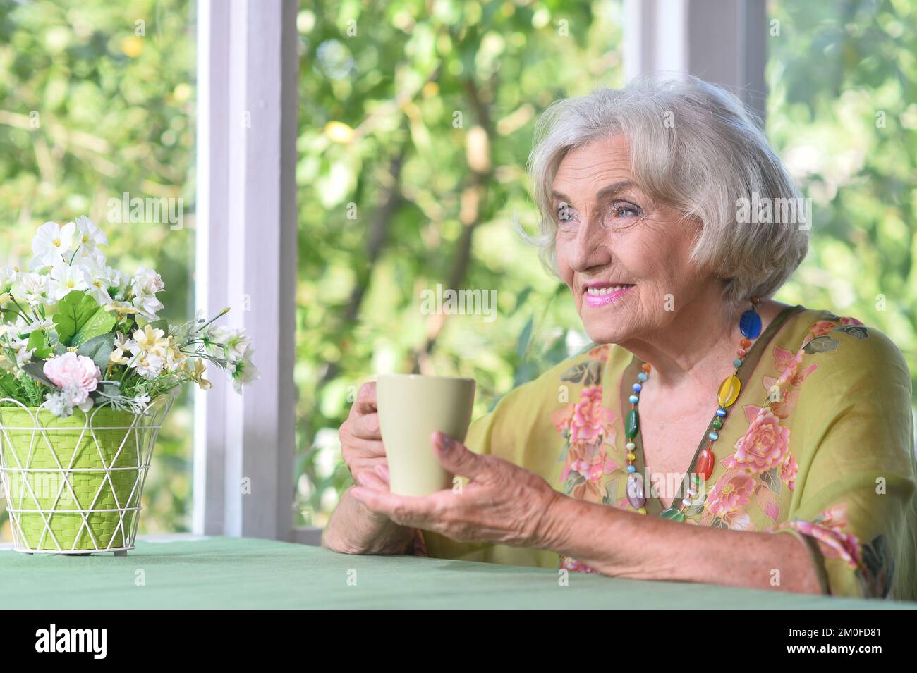 une vieille femme à une table et à boire du thé Banque D'Images