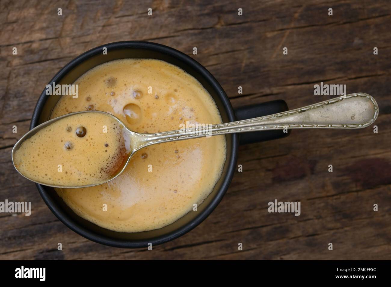 Tasse à espresso et cuillère noires avec mousse sur table en bois Banque D'Images